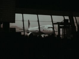 Silhouette of an airplane and waiting passengers inside an airport terminal at dusk.
