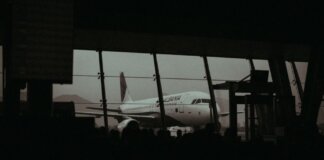 Silhouette of an airplane and waiting passengers inside an airport terminal at dusk.
