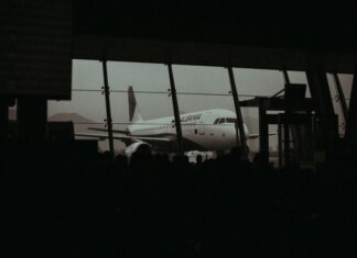 Silhouette of an airplane and waiting passengers inside an airport terminal at dusk.