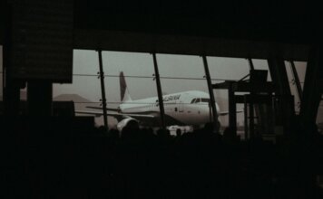 Консерваторы требуют от Air Canada обслуживать пассажиров на двух официальных языках Silhouette of an airplane and waiting passengers inside an airport terminal at dusk.