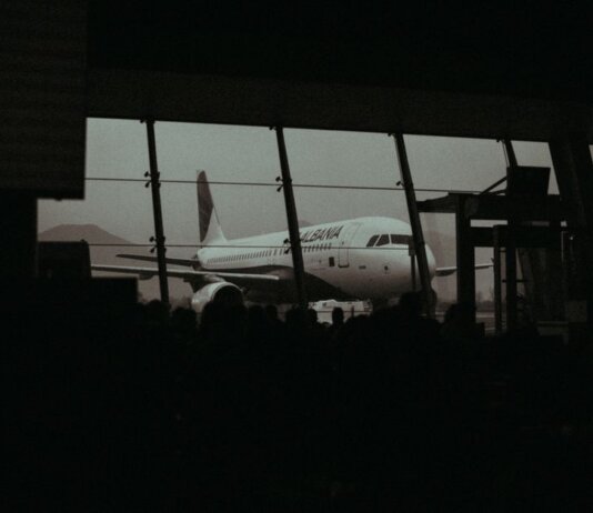 Silhouette of an airplane and waiting passengers inside an airport terminal at dusk.