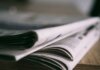Кризис местной журналистики в Канаде: спасёт ли её государственная поддержка? Stack of folded newspapers on a wooden table with a focus on printed pages.