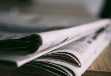 Stack of folded newspapers on a wooden table with a focus on printed pages.