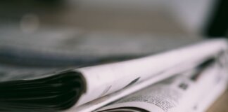 Stack of folded newspapers on a wooden table with a focus on printed pages.
