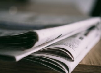 Кризис местной журналистики в Канаде: спасёт ли её государственная поддержка? Stack of folded newspapers on a wooden table with a focus on printed pages.