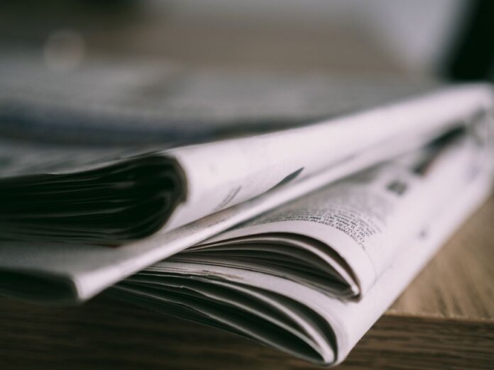 Stack of folded newspapers on a wooden table with a focus on printed pages. Stack of folded newspapers on a wooden table with a focus on printed pages.