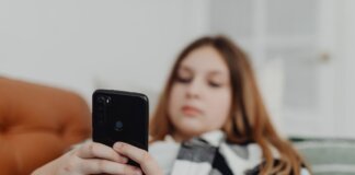 Teenage girl using smartphone while relaxing on a sofa, depicting leisure and connectivity.