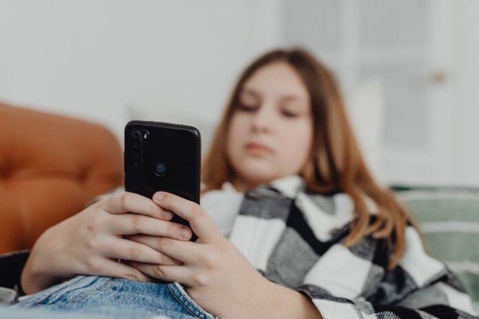 Teenage girl using smartphone while relaxing on a sofa, depicting leisure and connectivity. Teenage girl using smartphone while relaxing on a sofa, depicting leisure and connectivity.