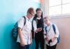 Instagram расширяет программу для школ: новые функции для учеников и родителей Three children in school uniforms using a smartphone, standing near a blue wall indoors.