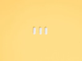 Three white capsules on a vibrant yellow background, symbolizing healthcare and medication.
