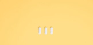 Three white capsules on a vibrant yellow background, symbolizing healthcare and medication.