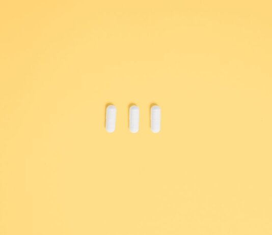 Three white capsules on a vibrant yellow background, symbolizing healthcare and medication.