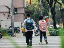 Two children with backpacks crossing a street at a pedestrian crossing.