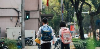 Two children with backpacks crossing a street at a pedestrian crossing.