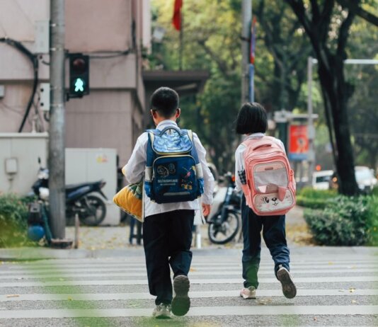Two children with backpacks crossing a street at a pedestrian crossing.
