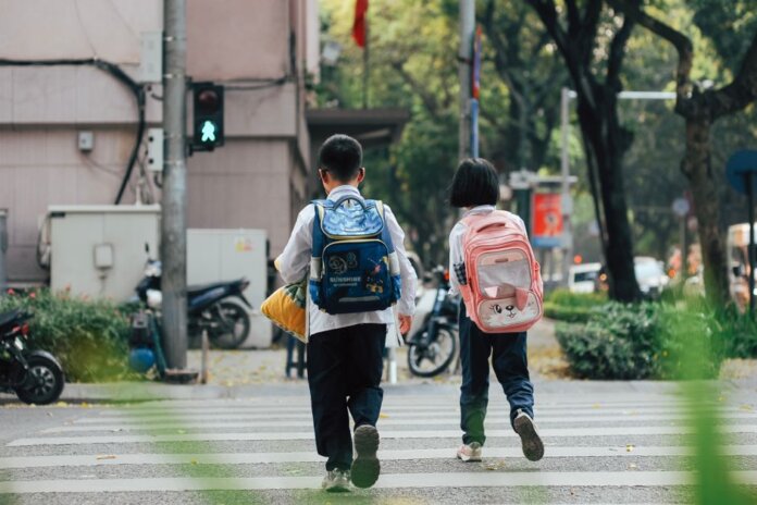 Two children with backpacks crossing a street at a pedestrian crossing. Two children with backpacks crossing a street at a pedestrian crossing.