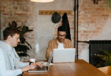 Two men working on laptops in a stylish office with exposed brick walls.