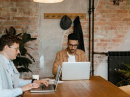 Two men working on laptops in a stylish office with exposed brick walls.