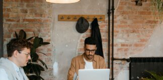 Two men working on laptops in a stylish office with exposed brick walls.