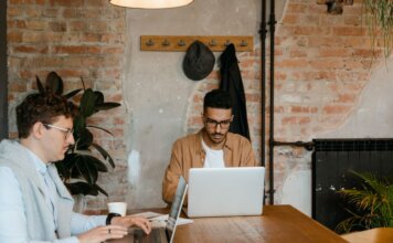 Two men working on laptops in a stylish office with exposed brick walls.