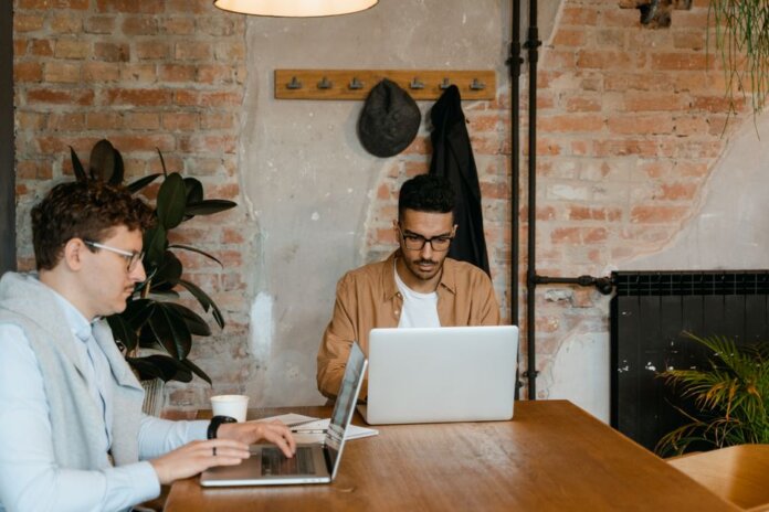 Two men working on laptops in a stylish office with exposed brick walls.