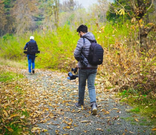 Two photographers walking down a leaf-covered forest path capturing nature's beauty.