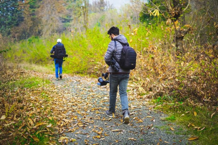 Two photographers walking down a leaf-covered forest path capturing nature's beauty.