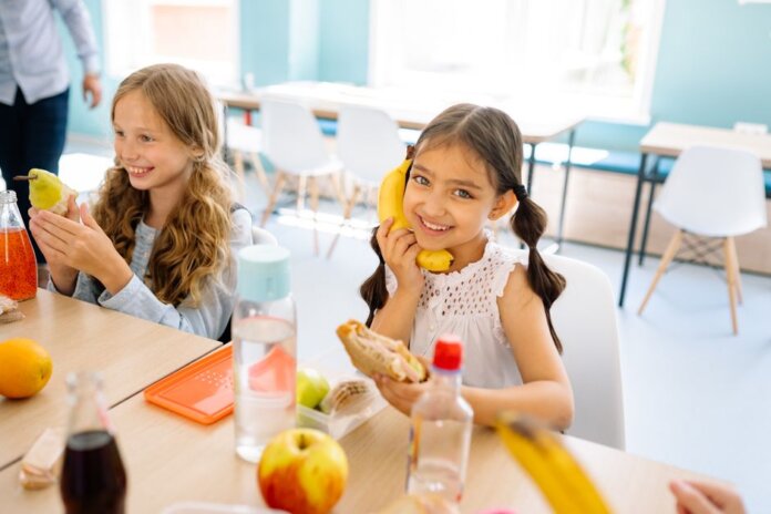 Two smiling girls enjoying snacks during break time in a school classroom. Two smiling girls enjoying snacks during break time in a school classroom.