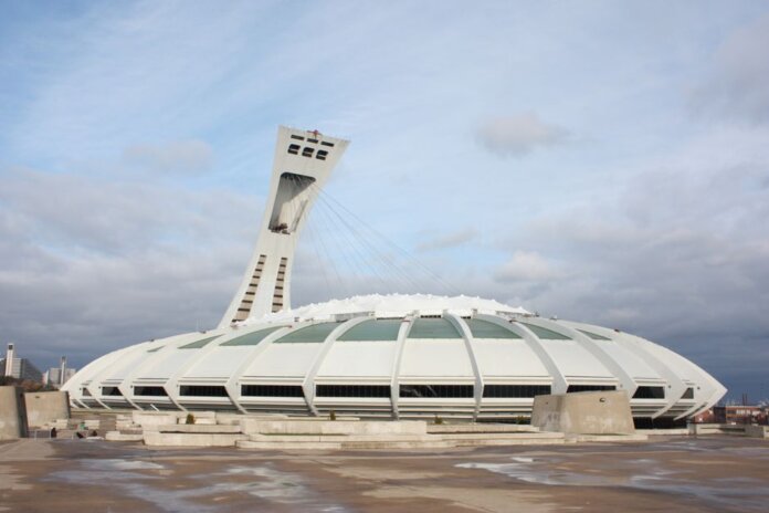 View of the iconic Olympic Stadium in Montreal, Canada, under a cloudy sky. View of the iconic Olympic Stadium in Montreal, Canada, under a cloudy sky.