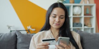Woman sitting on sofa shopping online with mobile and credit card.