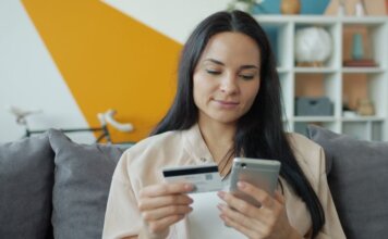Woman sitting on sofa shopping online with mobile and credit card.