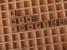Wooden Scrabble letters arranged to spell 'A New Chapter' on a gridded board.