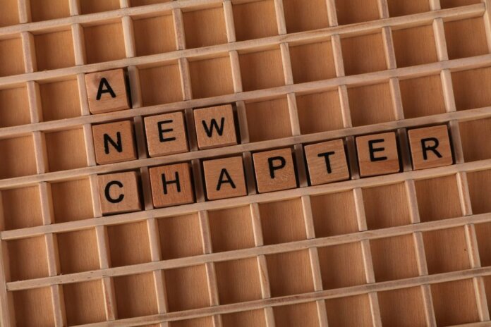 Wooden Scrabble letters arranged to spell 'A New Chapter' on a gridded board.
