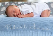 A baby sleeps peacefully on a blue knit blanket with name embroidery.