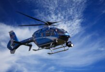 A blue police helicopter patrolling the sky on a clear sunny day.