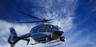 A blue police helicopter patrolling the sky on a clear sunny day.