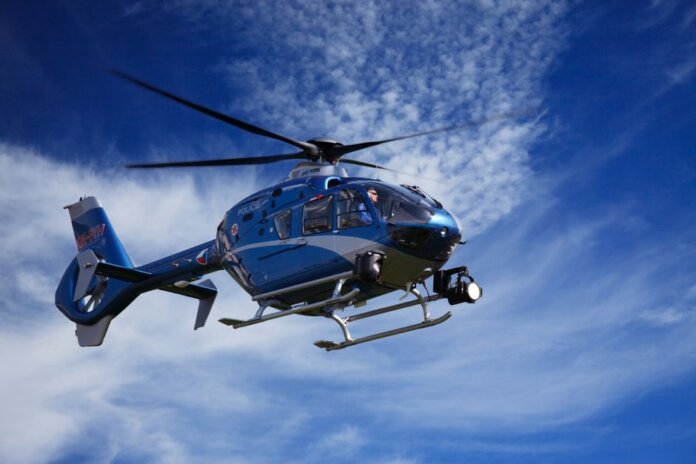 A blue police helicopter patrolling the sky on a clear sunny day.