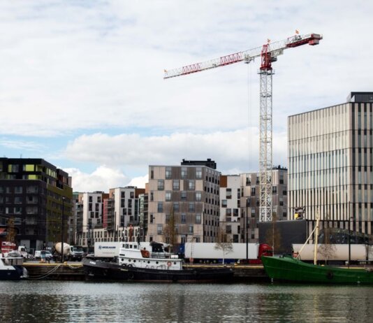 A cityscape featuring modern residential buildings and a construction crane by the waterfront.