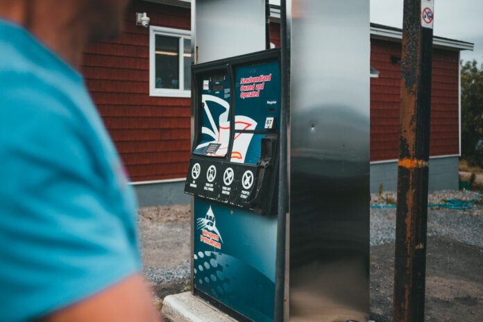 A close-up of a gas pump with a person nearby in Newfoundland, outdoors. A close-up of a gas pump with a person nearby in Newfoundland, outdoors.