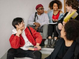 A diverse group of students sitting on stairs, smiling and collaborating indoors.