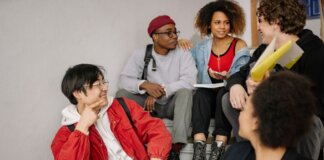 A diverse group of students sitting on stairs, smiling and collaborating indoors.