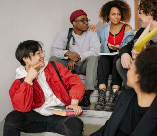A diverse group of students sitting on stairs, smiling and collaborating indoors.