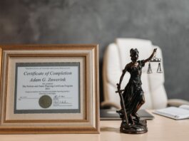 A framed legal certificate and Lady Justice figurine on a desk in a law office setting.