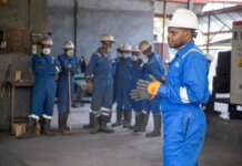 A group of factory workers in safety gear receiving training indoors.