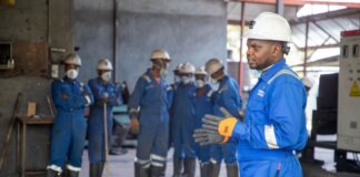 A group of factory workers in safety gear receiving training indoors.