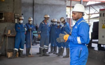 A group of factory workers in safety gear receiving training indoors.