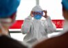 A healthcare professional dons protective clothing at an airport, highlighting safety measures during a pandemic.