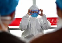 A healthcare professional dons protective clothing at an airport, highlighting safety measures during a pandemic.