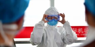 A healthcare professional dons protective clothing at an airport, highlighting safety measures during a pandemic.