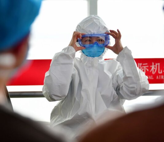 A healthcare professional dons protective clothing at an airport, highlighting safety measures during a pandemic.
